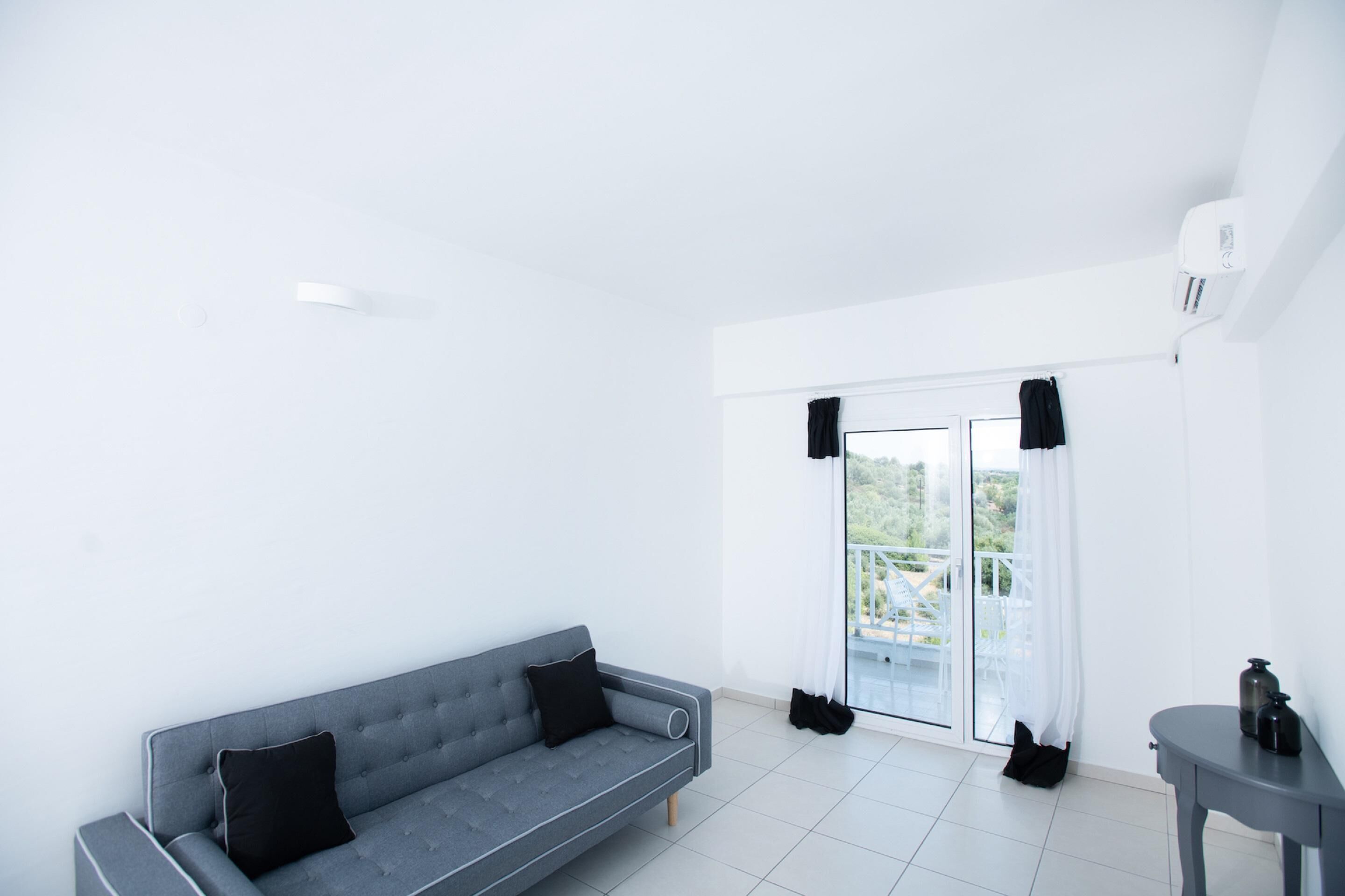 Et moderne, minimalistisk værelse med en grå sofa, et lille bord og en skydedør af glas, der fører til en udendørs balkon.