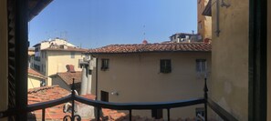 A balcony with a view of terracotta-tiled buildings, a clear blue sky, and a railing. - Vecchia Volta (Florence)