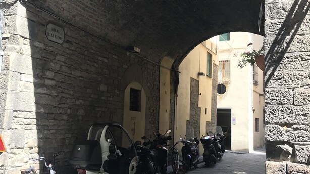 An arched stone bridge with parked motorcycles and bicycles on the street below. - Vecchia Volta (Florence)