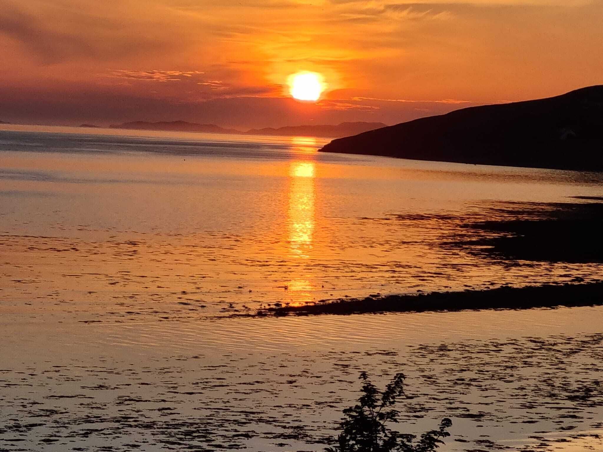 A sunset over a calm body of water with a silhouette of a mountain in the background.