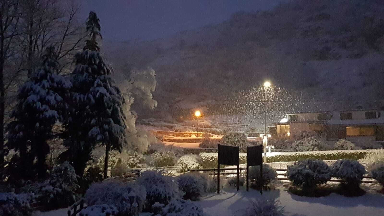 A snow-covered landscape with a lit building in the background.