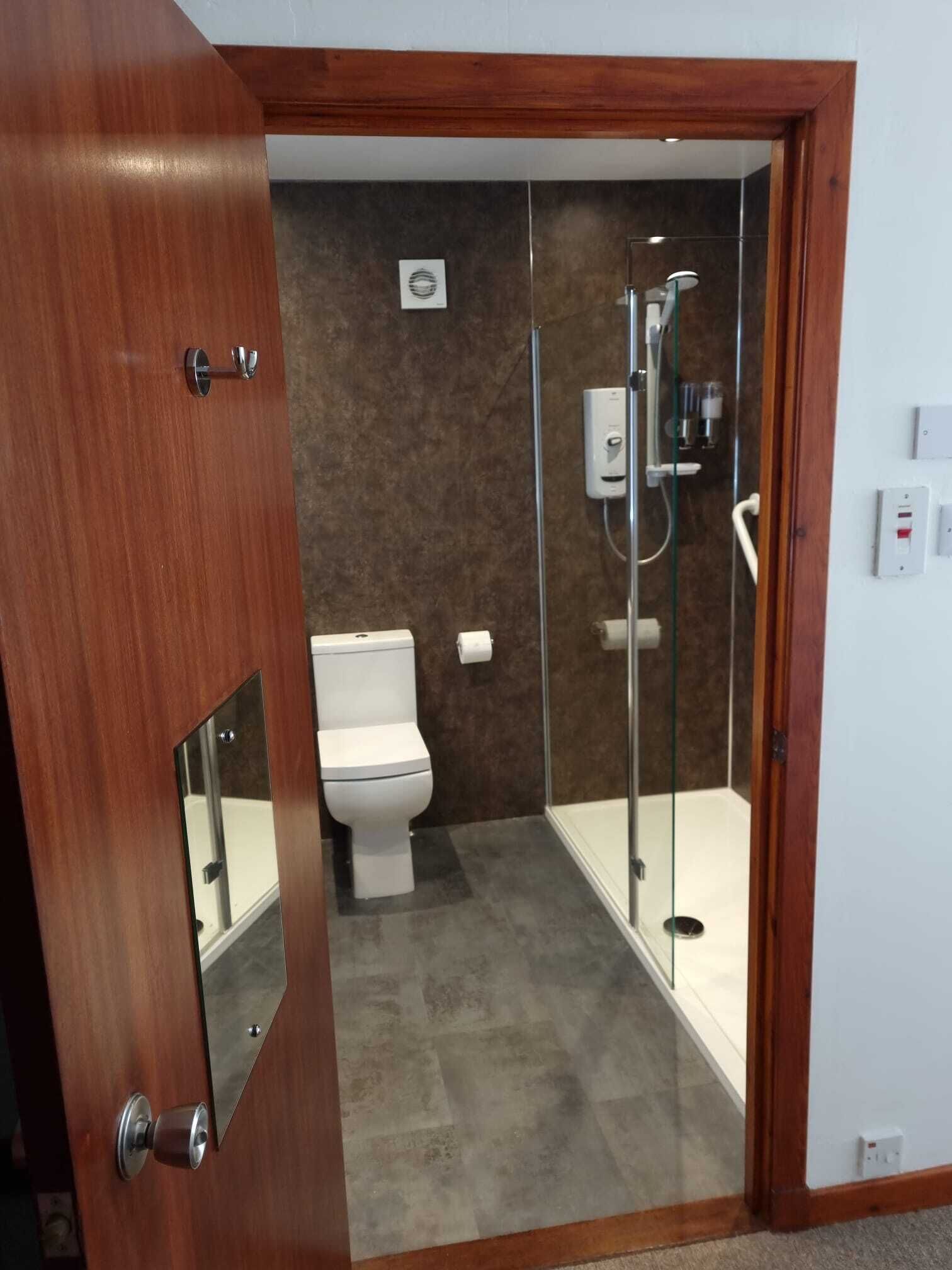 Une salle de bain avec des toilettes, une douche en verre et une porte en bois.