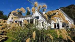 A white house with a gabled roof and a visible chimney, surrounded by tall grasses and a clear blue sky. - Lochview Guest House (Ullapool)