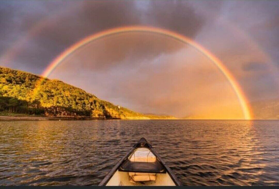 A boat on calm water with a rainbow in the background.