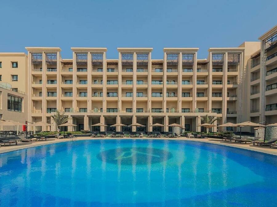 A hotel with a large swimming pool, multiple balconies, and sun loungers.