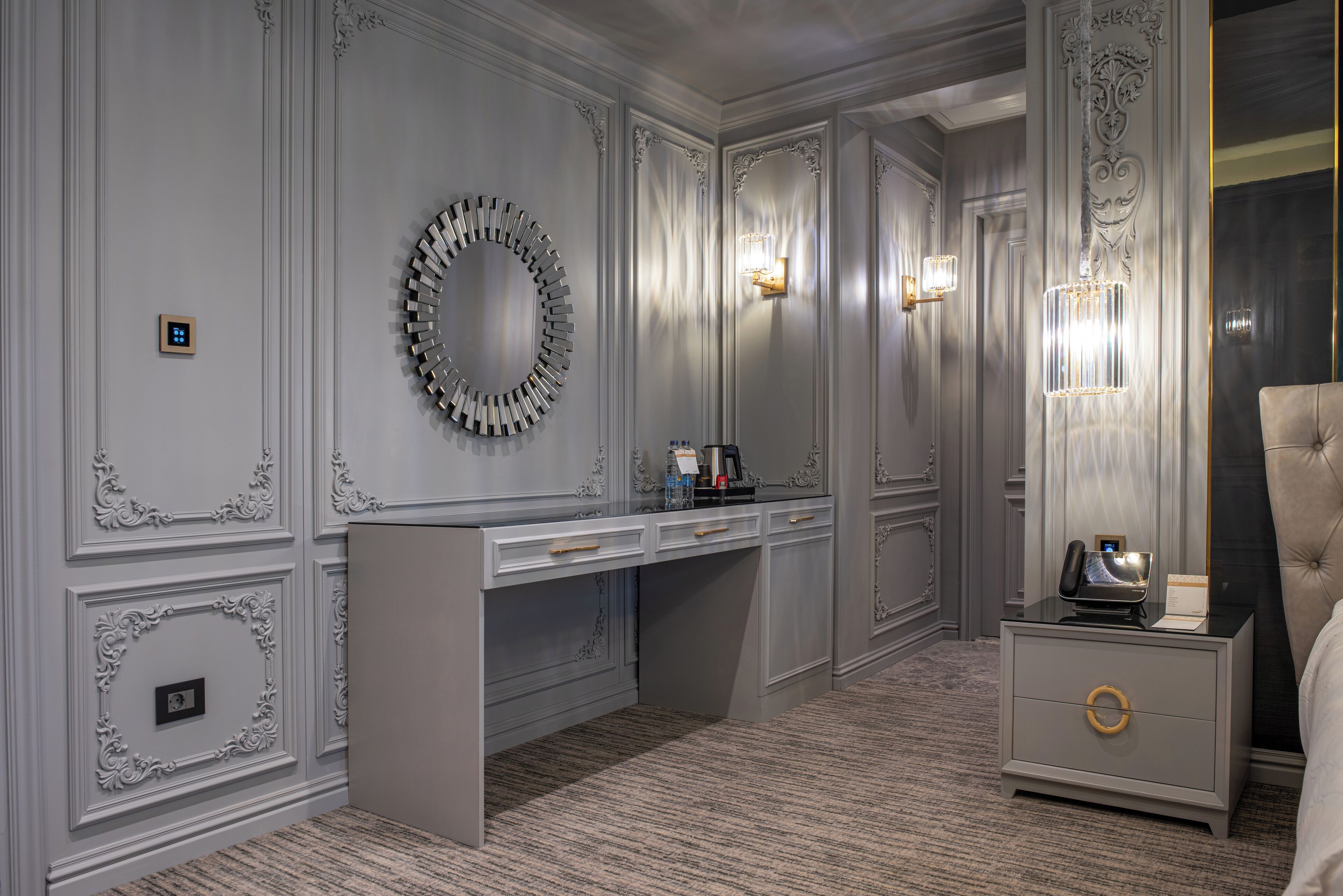 A hotel room with a vanity, a mirror, a desk, and a nightstand.