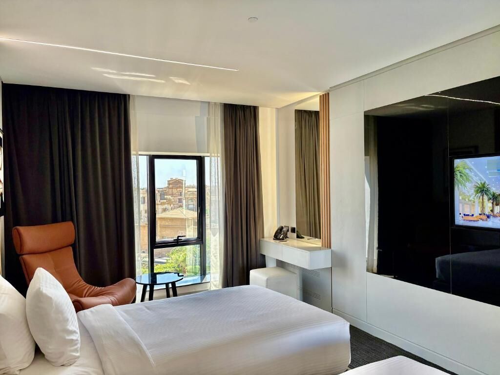 A hotel room with a large bed, a desk, a chair, and a television.