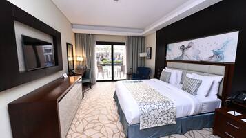 Quarto de hotel com uma cama grande, uma escrivaninha, uma cadeira, televisão e vista para o exterior.