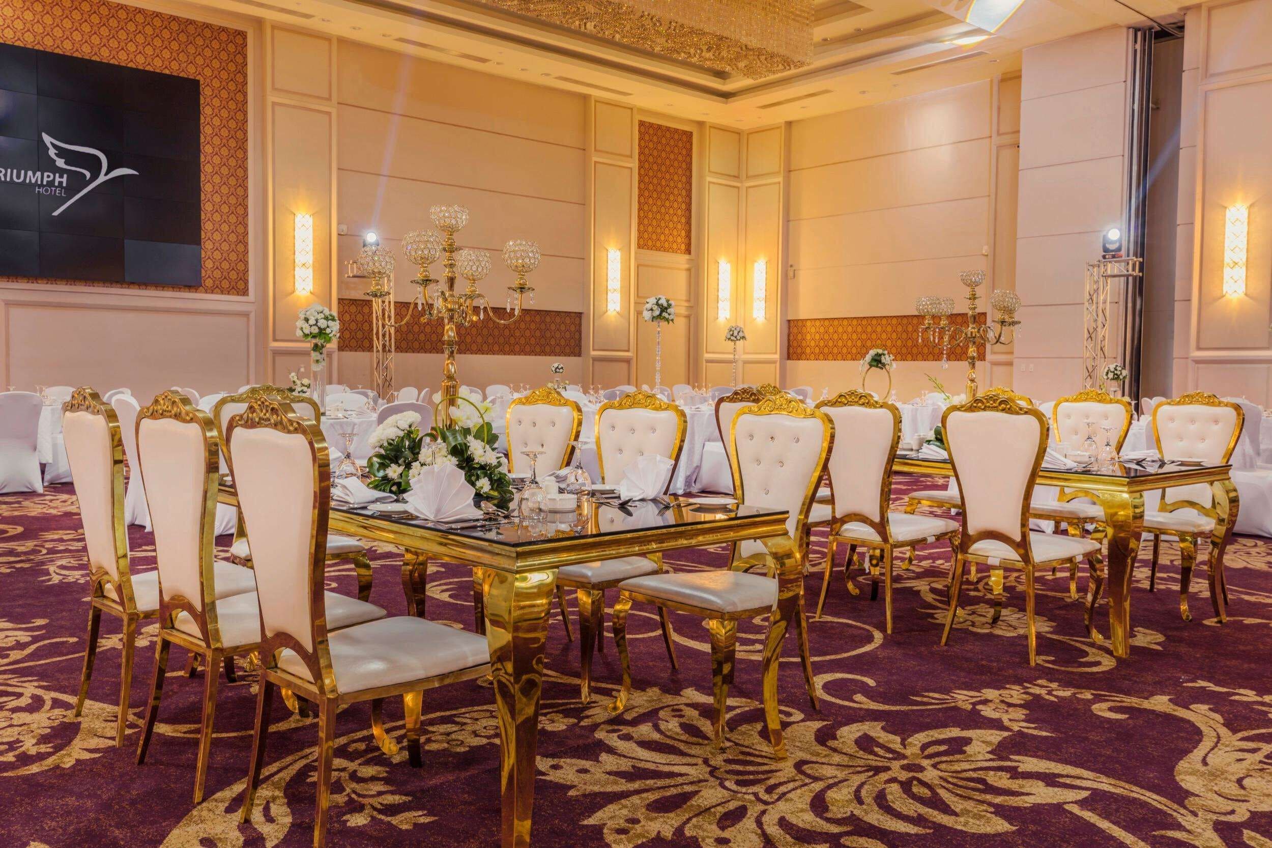 A banquet hall with round tables, gold chairs, and white tablecloths.
