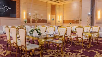 A banquet hall with round tables, gold chairs, and white tablecloths.