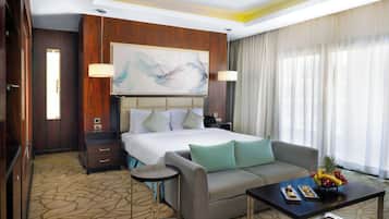 A hotel room with a large bed, a sofa, a coffee table with fruit, and a painting on the wall.