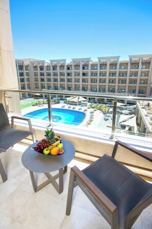 Un balcón con una mesa que sostiene fruta y vistas a una piscina y edificios de hotel.