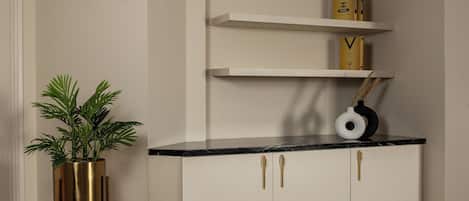 A corner room with a white cabinet, a black marble countertop, and a gold plant stand.