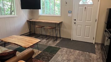 A room with a wooden table, two bar stools, a television mounted on the wall, and a door with a window.