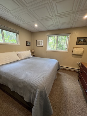 Relax in this serene bedroom with a large bed, two windows, and a beautiful view of the surrounding greenery.