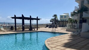 Una piscina cristalina con una terraza de madera y sillones de descanso, una pérgola y vistas al océano.