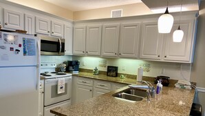 Una cocina con armarios blancos, encimera de granito, electrodomésticos de acero inoxidable e iluminación colgante.