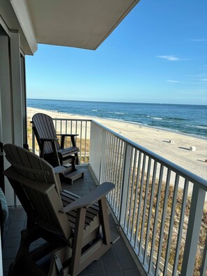Un balcon avec deux fauteuils Adirondack et une petite table, donnant sur une plage de sable et l’océan.