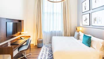 Ein Hotelzimmer mit einem Bett, einem Schreibtisch mit Fernseher, einem Stuhl und einem Fenster mit Vorhängen.