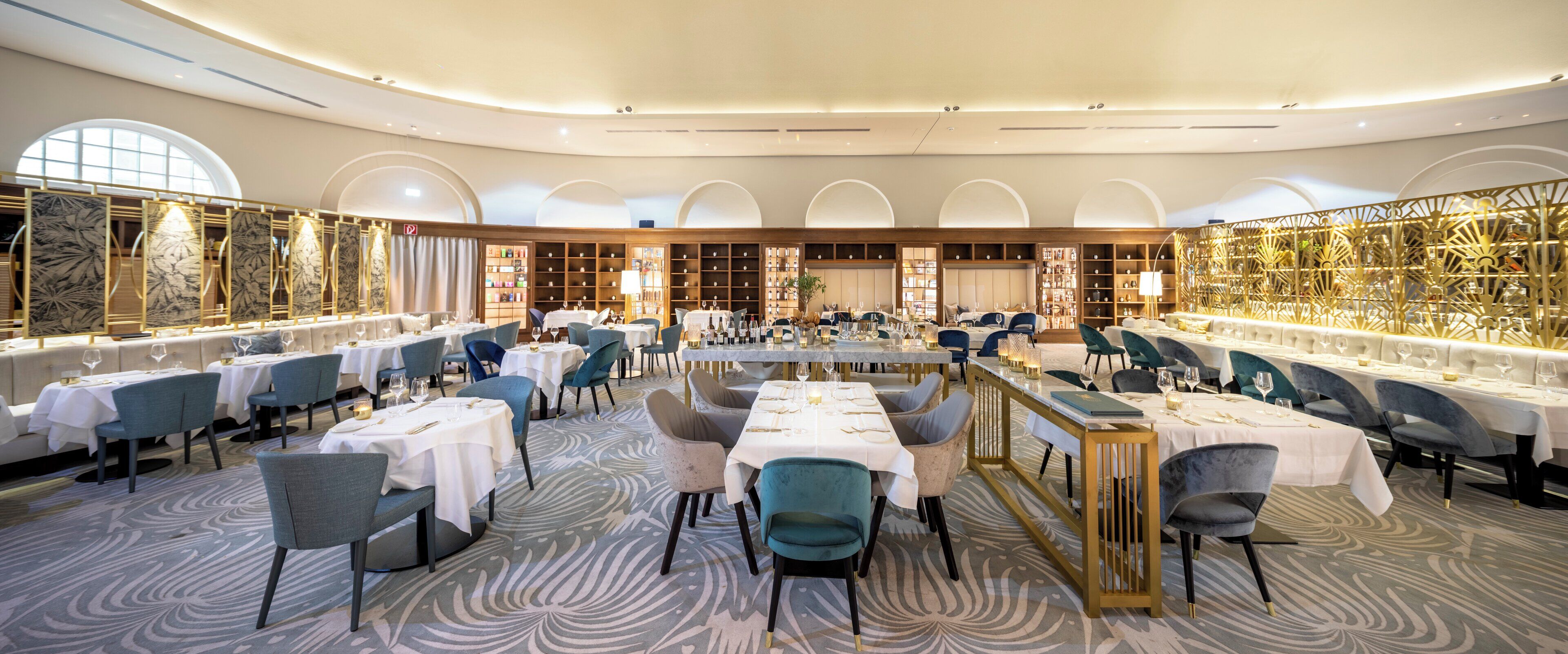 A spacious dining area with multiple tables and chairs, a patterned carpet, and a decorative wall with shelves.