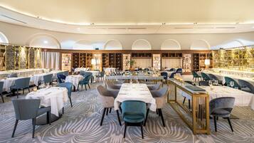 A spacious dining area with multiple tables and chairs, a patterned carpet, and a decorative wall with shelves.