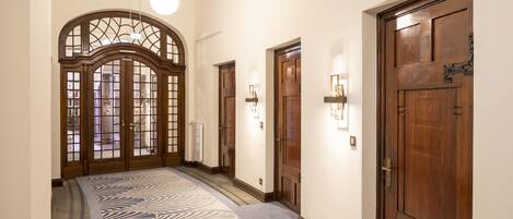 A hallway with a patterned carpet, wooden doors, and wall-mounted light fixtures.