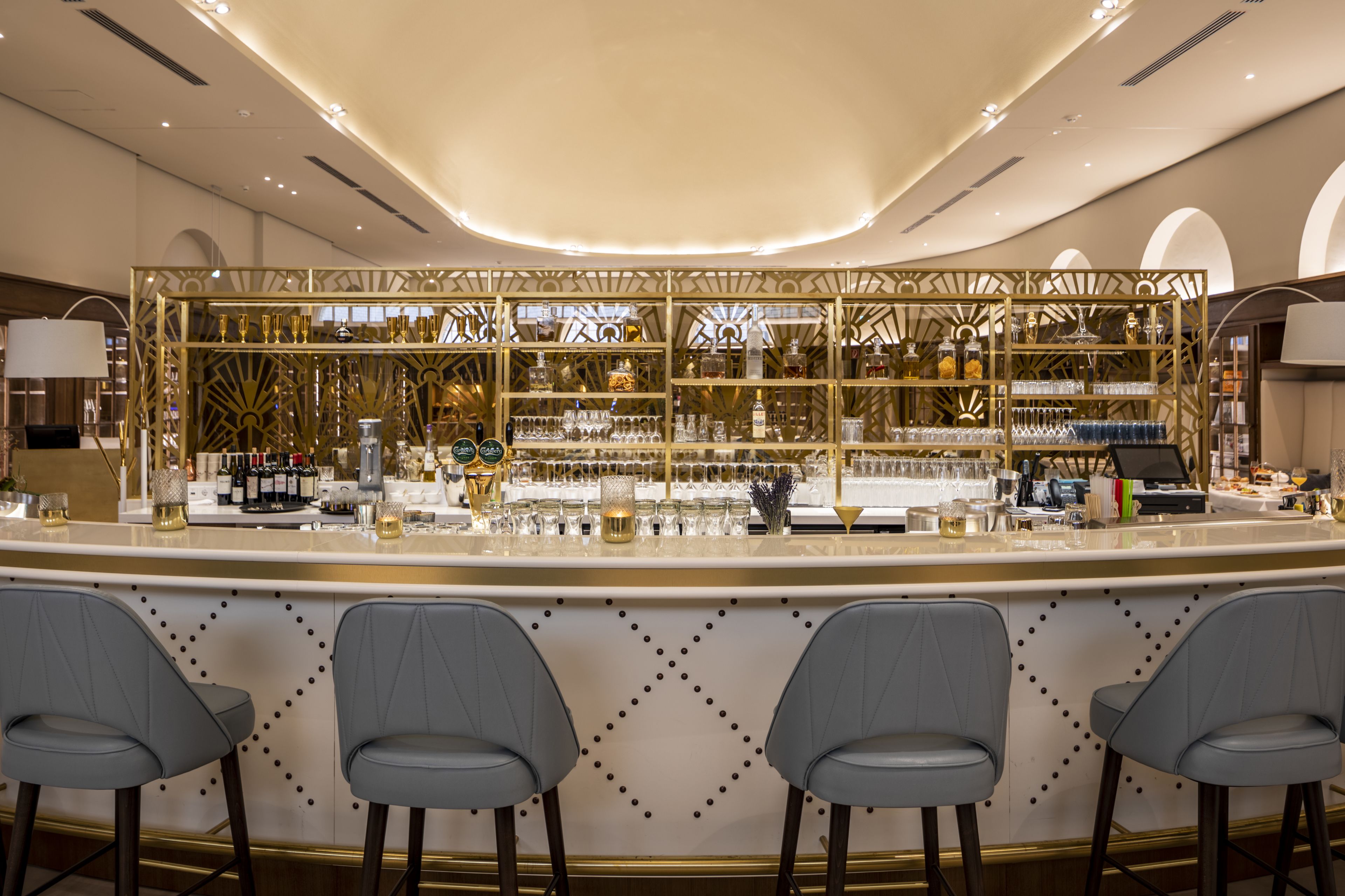 Eine Bar mit einer Theke, Barhocker und Regalen voller Flaschen und Gläser.
