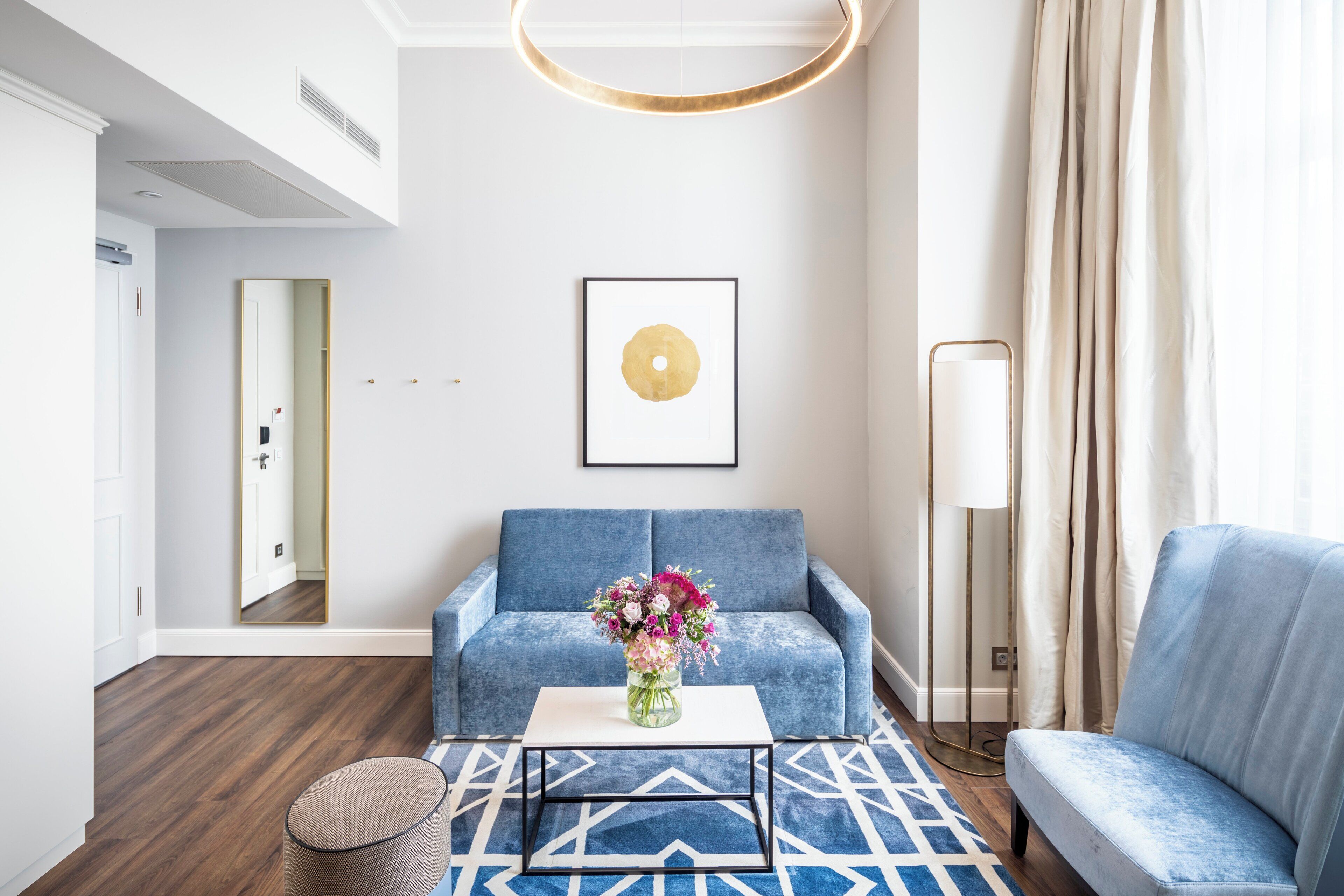 A modern living room with a blue sofa, a white coffee table, and a vase of flowers.