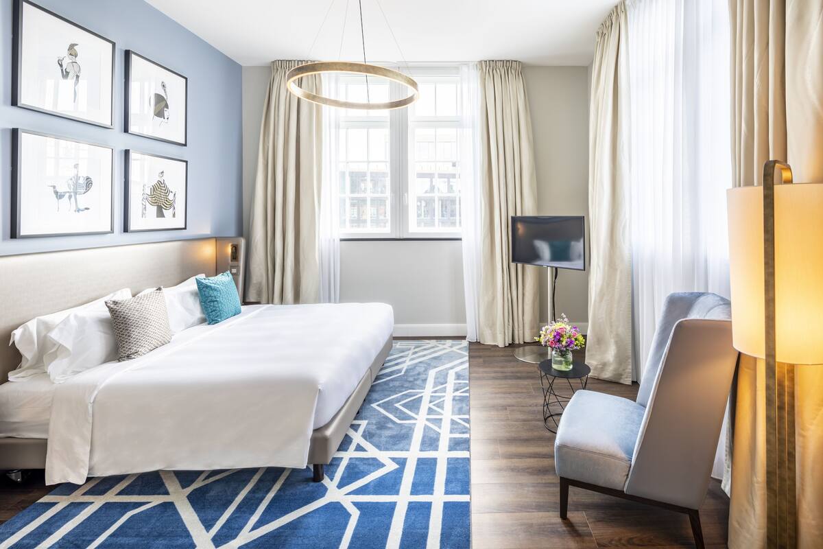 A hotel room with a large bed, a TV, a chair, and a window with curtains.