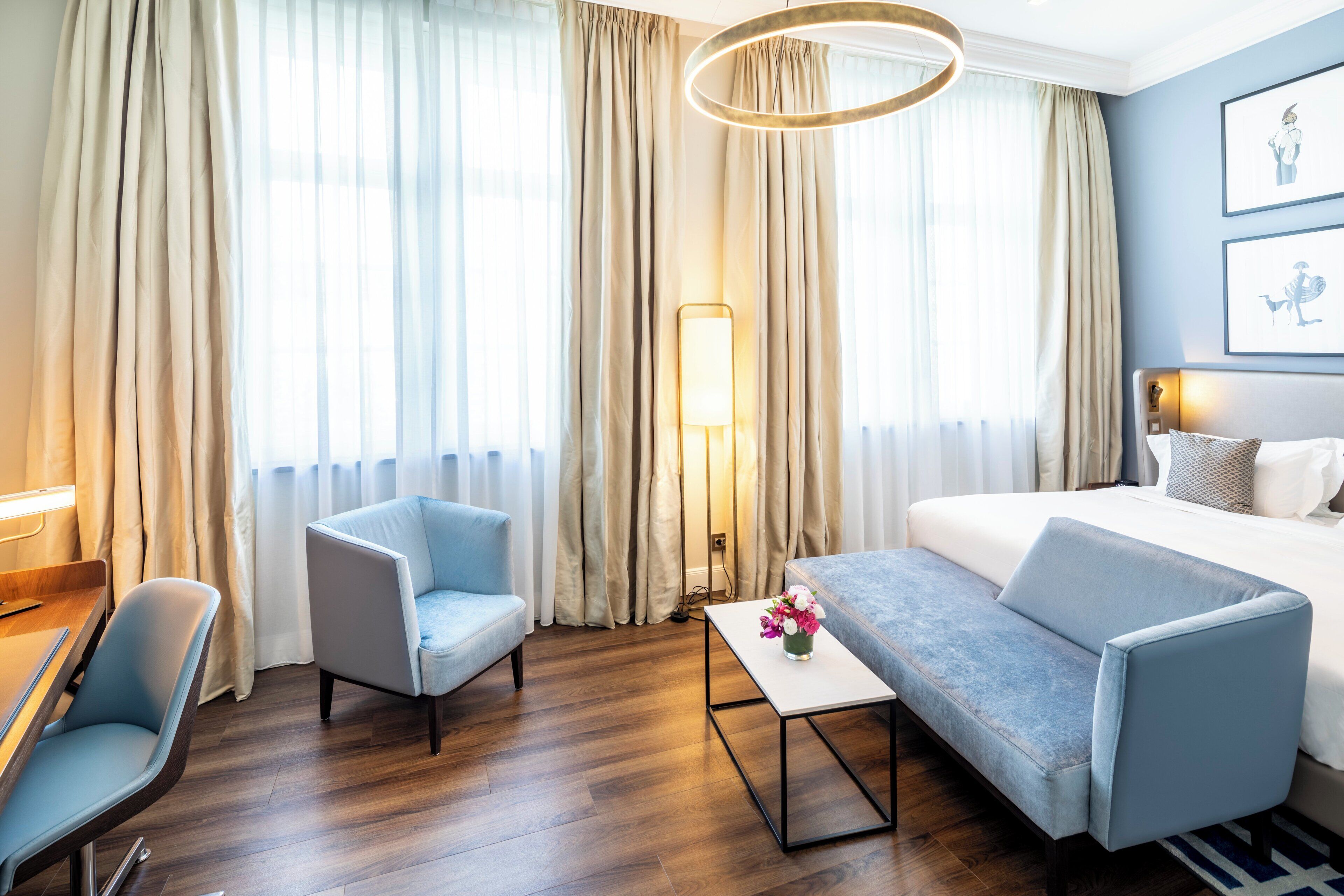 A hotel room with a bed, a sofa, a chair, a small table, and a lamp.