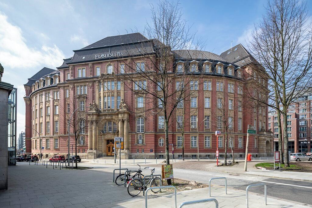 A historic building with a red facade and classical architecture, featuring a prominent entrance and a sign reading "FRASERS SUITES."