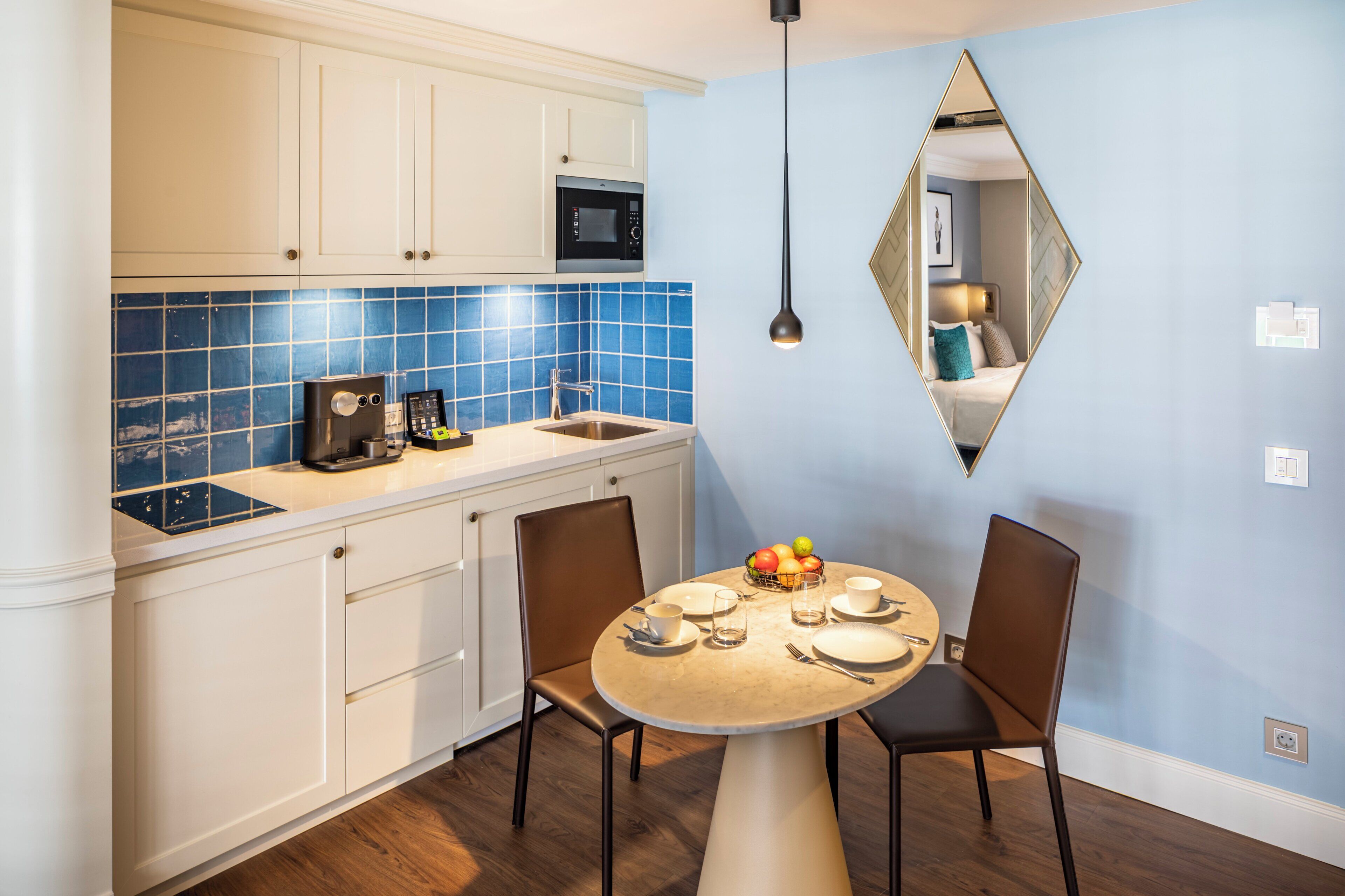 A modern kitchen with white cabinets, a blue tiled backsplash, and a dining area with a round table and two chairs.