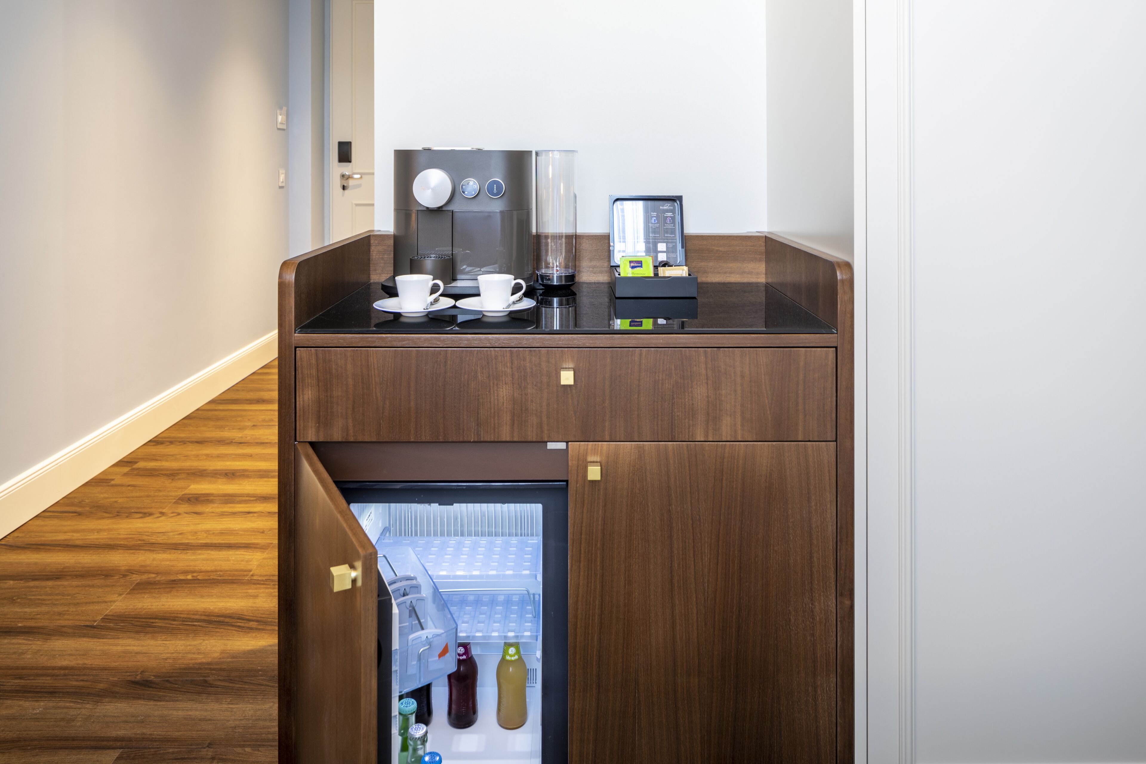 Una kitchenette compacta con cafetera, un refrigerador pequeño y una máquina de café.
