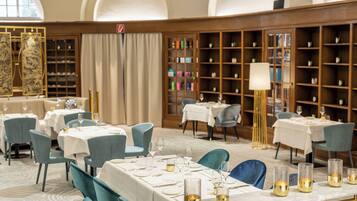 A dining area with tables set for service, a large bookshelf, and a decorative lamp.
