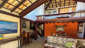 A spacious living area with a high ceiling, a large sofa, a coffee table, and a television. - Linda casa a 150 mts da Praia Ferradura (Búzios)