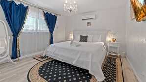 Une chambre d’hôtel avec un grand lit, des rideaux blancs, un lustre, une petite table de chevet avec une lampe et un tableau au mur.