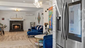 Un salon moderne avec une cheminée, des fauteuils bleus, une table basse en marbre et un réfrigérateur en acier inoxydable.