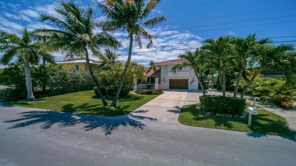 A residential property with a well-maintained lawn, palm trees, and a driveway leading to a garage. - March Availability, Beach, 70 ft Dock - Marathon VACA-23-16 Entire House (Marathon)