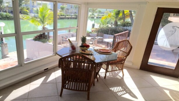 Un coin repas avec une table en verre et des chaises en osier, donnant sur une piscine et un espace verdoyant.