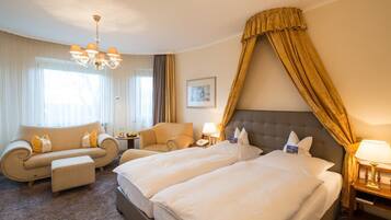 A hotel room with two beds, a sofa, a chair, a chandelier, and a large window with curtains.