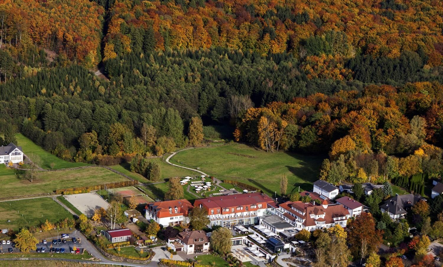 An aerial view of a residential area with houses, a large building with a red roof, and a green field.