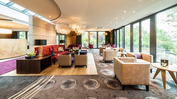 Un hall d’entrée spacieux au design moderne, avec un canapé rouge, plusieurs fauteuils et un grand lustre.