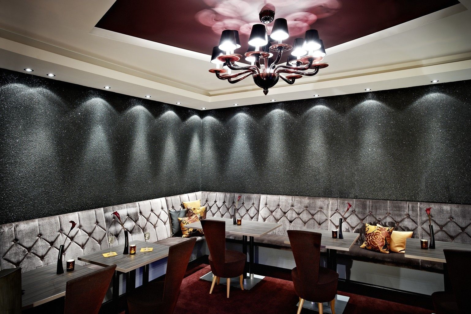 A corner seating area with a tufted headboard, a chandelier, and a dark textured wall.