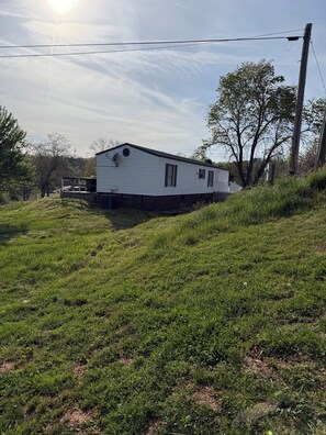 Una casa móvil con antena parabólica, rodeada de terreno cubierto de césped y árboles.