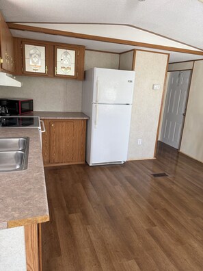 Una cocina compacta con armarios de madera, un refrigerador blanco, un microondas y un lavamanos.
