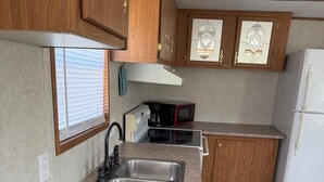 A compact kitchen with wooden cabinets, a stainless steel sink, a microwave, and a refrigerator. - Book longer and save weekly plus monthly discounts (Hayesville)