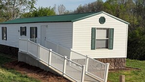 A single-story mobile home with a green roof, white exterior, and a small porch with a white railing. - Book longer and save weekly plus monthly discounts (Hayesville)