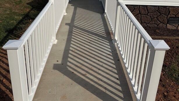 A concrete pathway leading to a white house with a stone foundation, surrounded by trees and utility poles. - Book longer and save weekly plus monthly discounts (Hayesville)
