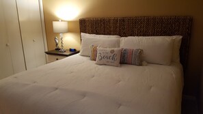 Una cama bien hecha con sábanas blancas y dos almohadas decorativas, una con motivos playeros.