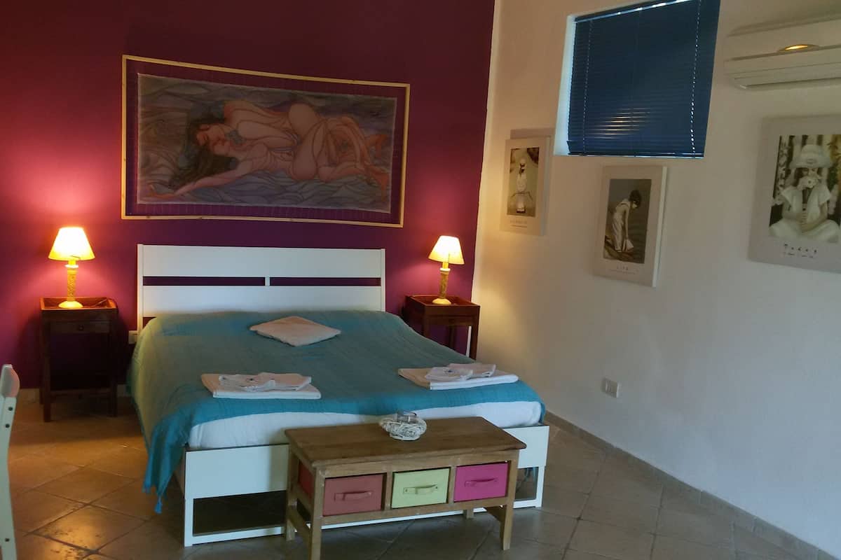 Ein Schlafzimmer mit einem Bett, zwei Nachttischen mit Lampen, einer kleinen Holzbänkschranke, einem Sessel und einem Bild an der Wand.